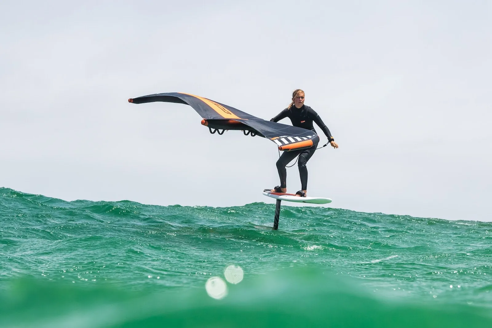 Rider de wingfoil volando sobre el agua con un ala naranja y gris